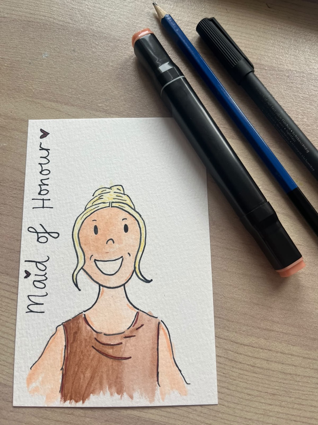 Watercolour doodle of the maid of honour in a brown dress, hair in a bun, lettered “Maid of Honour”